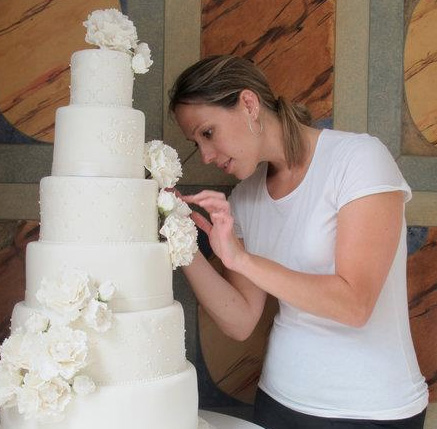 Wendy working on a six tier white wedding cake with peonies.